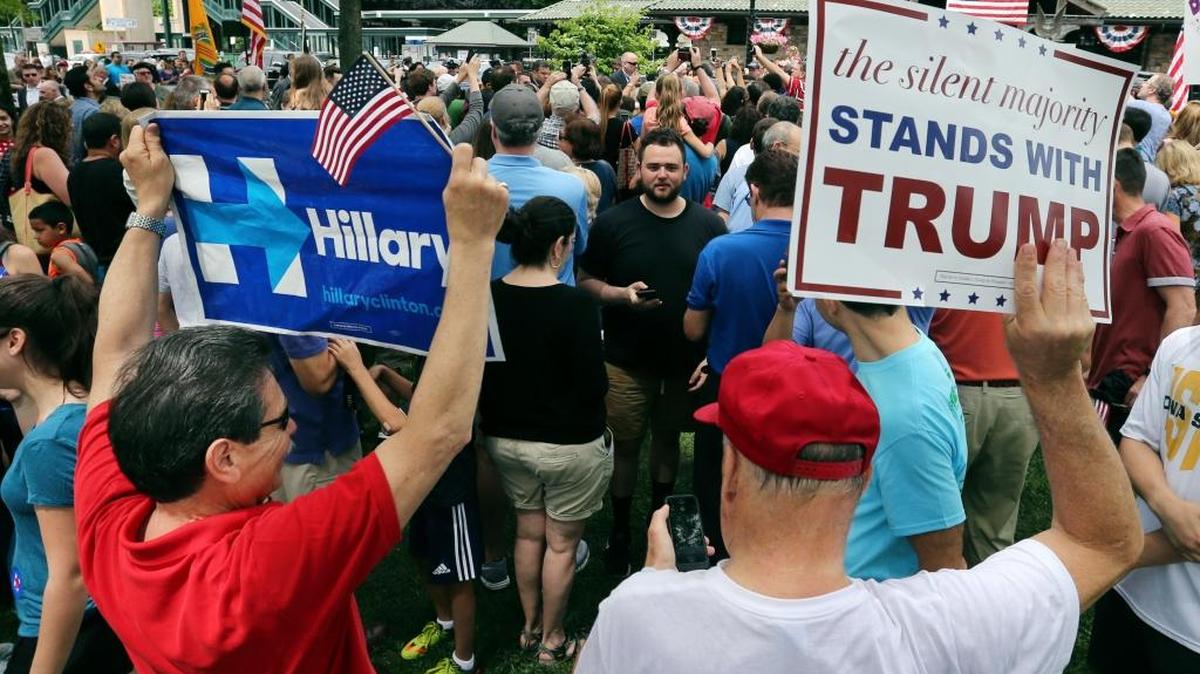 A supporter of Democratic presidential candidate Hillary Clinton and a Republican presidential candidate Donald Trump supporter hold signs as they attend a Memorial Day parade Monday, May 30, 2016, in Chappaqua, N.Y. Clinton and her husband former President Bill Clinton, along with New York Gov. Andrew Cuomo, walked in the parade.
