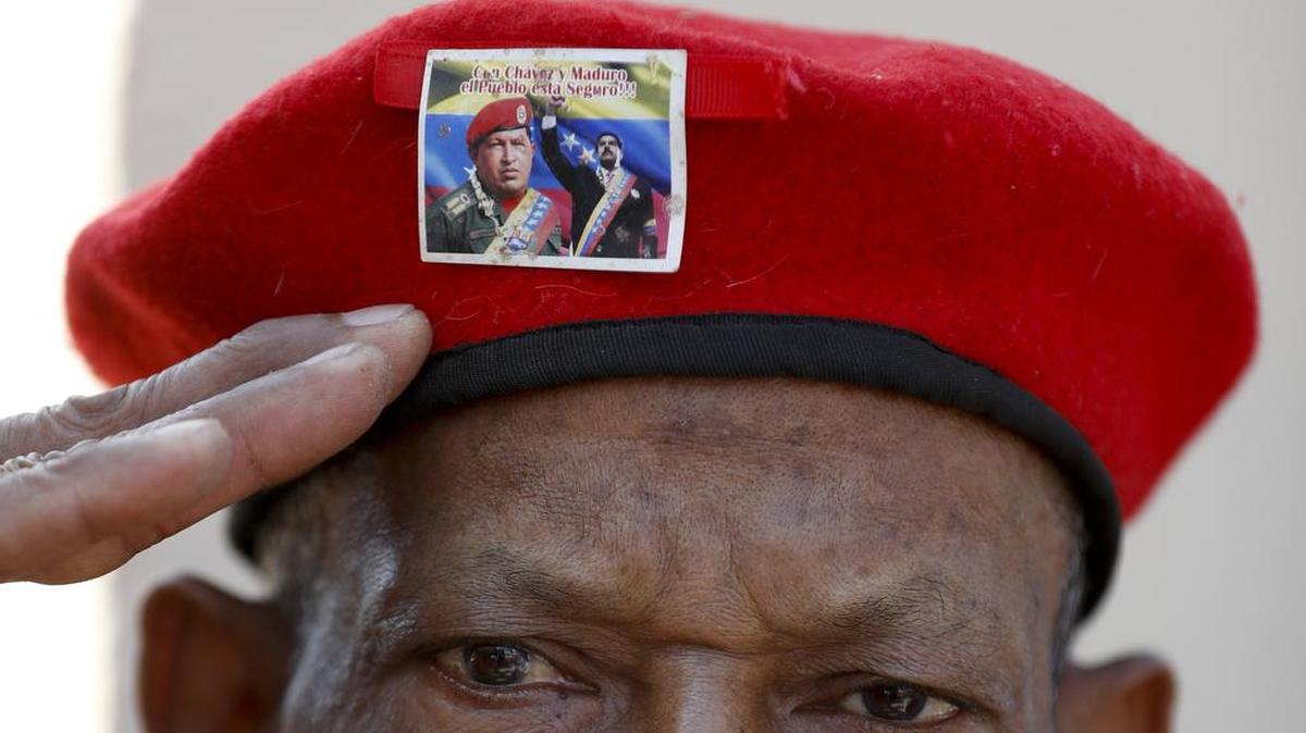 A man wearing the iconic red beret of Venezuela's late President Hugo Chavez, featuring a photo of current President Nicolas Maduro with Chavez, salutes as he waits to enter the Historic Military Museum to visit the leader's remains on the sixth anniversary of his death in Caracas, Venezuela, Tuesday, March 5, 2019. President Chavez was eventually allowed unprecedented powers. A reader says that President Trump may attempt to establish an oligarchy led by the absurdly rich, rather than a socialist state.