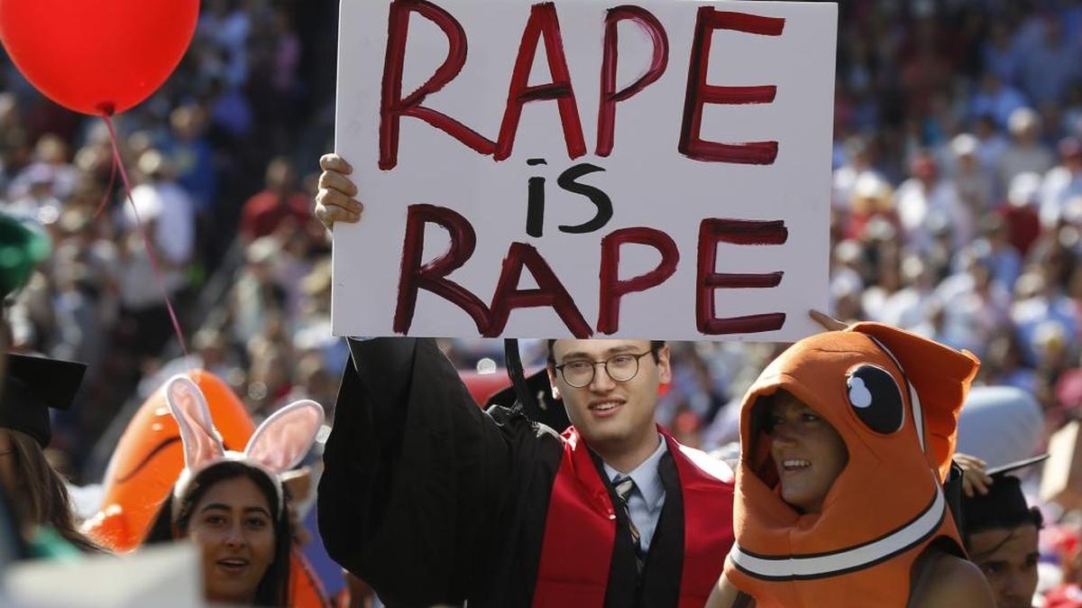 Paul Harrison, center, carries a sign of protest during Stanford University graduation exercises at Stanford Stadium, Sunday, June 12, 2016, in Stanford, Calif. A group of women's rights advocates are urging a California agency to take action against the judge who sentenced a former Stanford University swimmer to six months in jail for sexually assaulting an unconscious woman.
