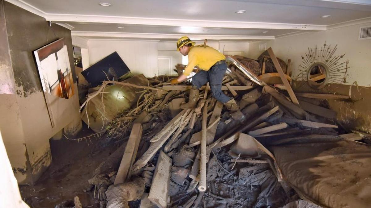In this Saturday, Jan. 13, 2018 photo provided by the Santa Barbara County Fire Department, Santa Barbara County Firefighter Vince Agapito searches through a Montecito, Calif., home that was destroyed by deadly mudflow and debris early Tuesday morning following heavy rainfall.