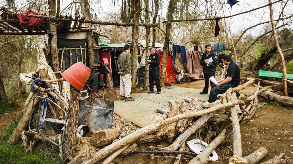 Detective Eric Azarvand, center, and community services officer Alissa Reina meet with two occupants of a large camp structure in the Salinas riverbed as they and other members of the Paso Robles Police Department make contact with folks living in the homeless camps along the Salinas in March.