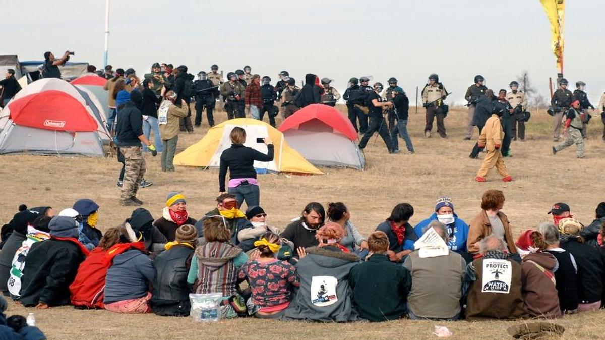Dakota Access Pipeline protesters sit in a prayer circle at the Front Line Camp on Oct. 27 as a line of law enforcement officers make their way across the camp to remove the protesters and relocate to the overflow camp a few miles to the south on Highway 1806 in Morton County, N.D. Members of more than 200 tribes from across North America have come to the Standing Rock Sioux Tribe’s encampment at the confluence of the Missouri and Cannonball rivers since August, the tribe says.