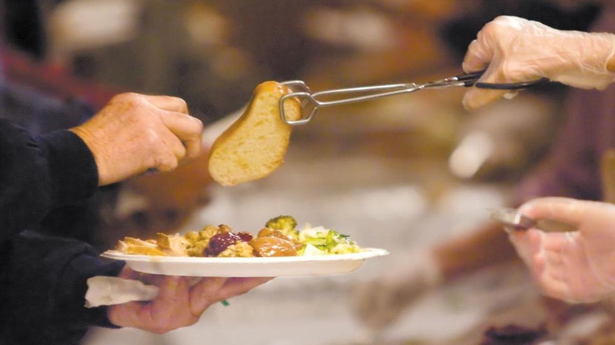 A volunteer serves a piece of fresh bread to a homeless person during a Christmas dinner at the Odd Fellows Hall in SLO in 2009.
