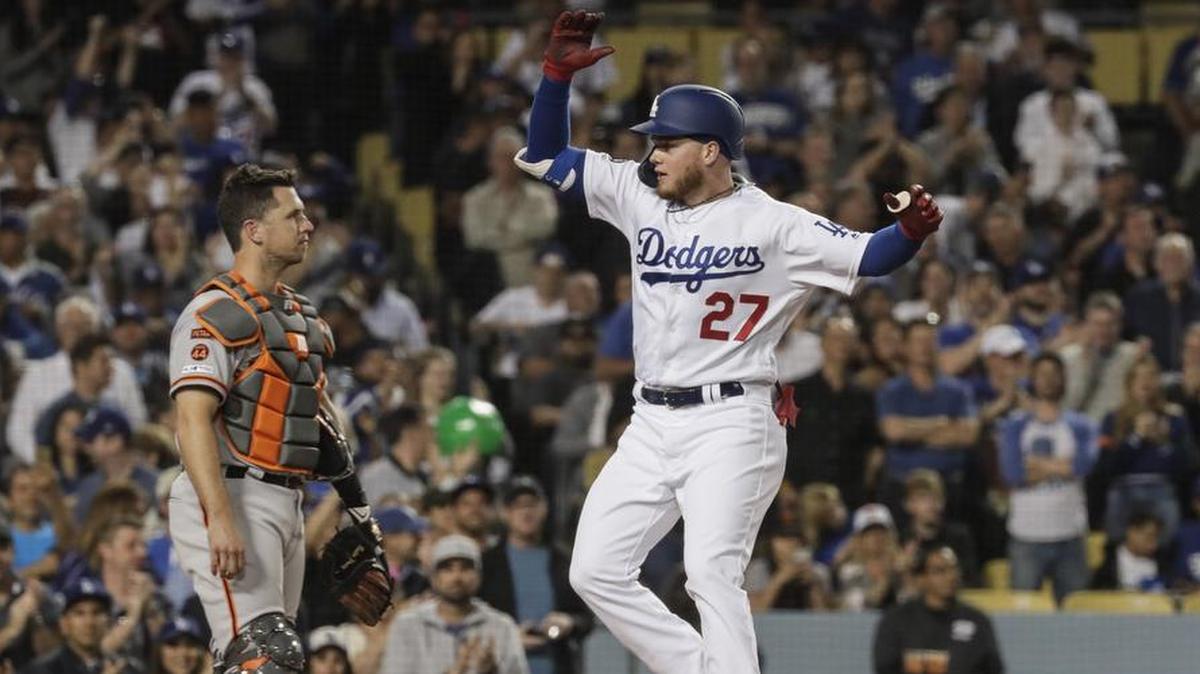 Central Coast sports fans are divided in their loyalties between Dodgers and Giants. Here, Dodger Alex Verdugo leaps at the plate after a 5th inning homer as Giants catcher Buster Posey looks on at Dodger Stadium on April 1, 2019.