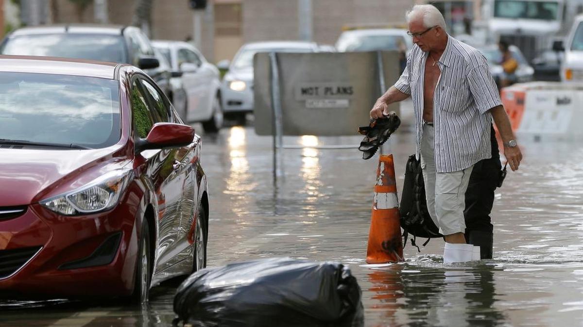 A hotel guest carries his shoes as he is escorted to his car in Miami Beach, Fla., on Sept. 30, 2015, as high tides flood the street.