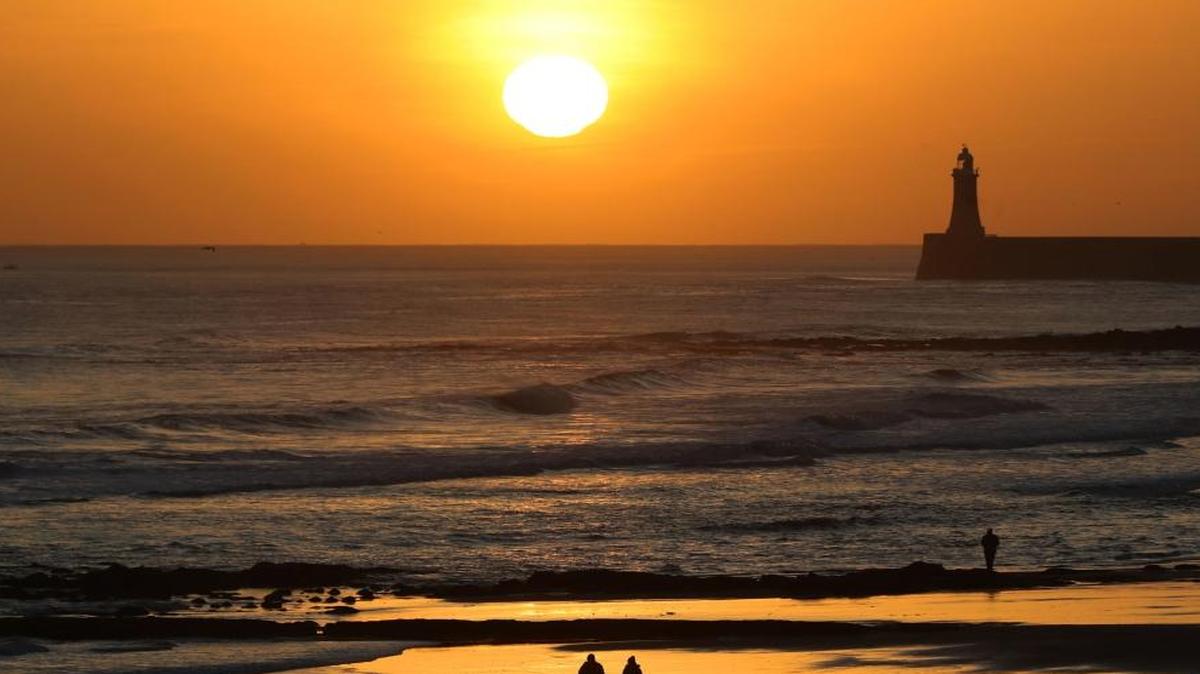 Walkers take a stroll along Tynemouth Longsands beach at sunrise on the northeast coast of England early Tuesday.