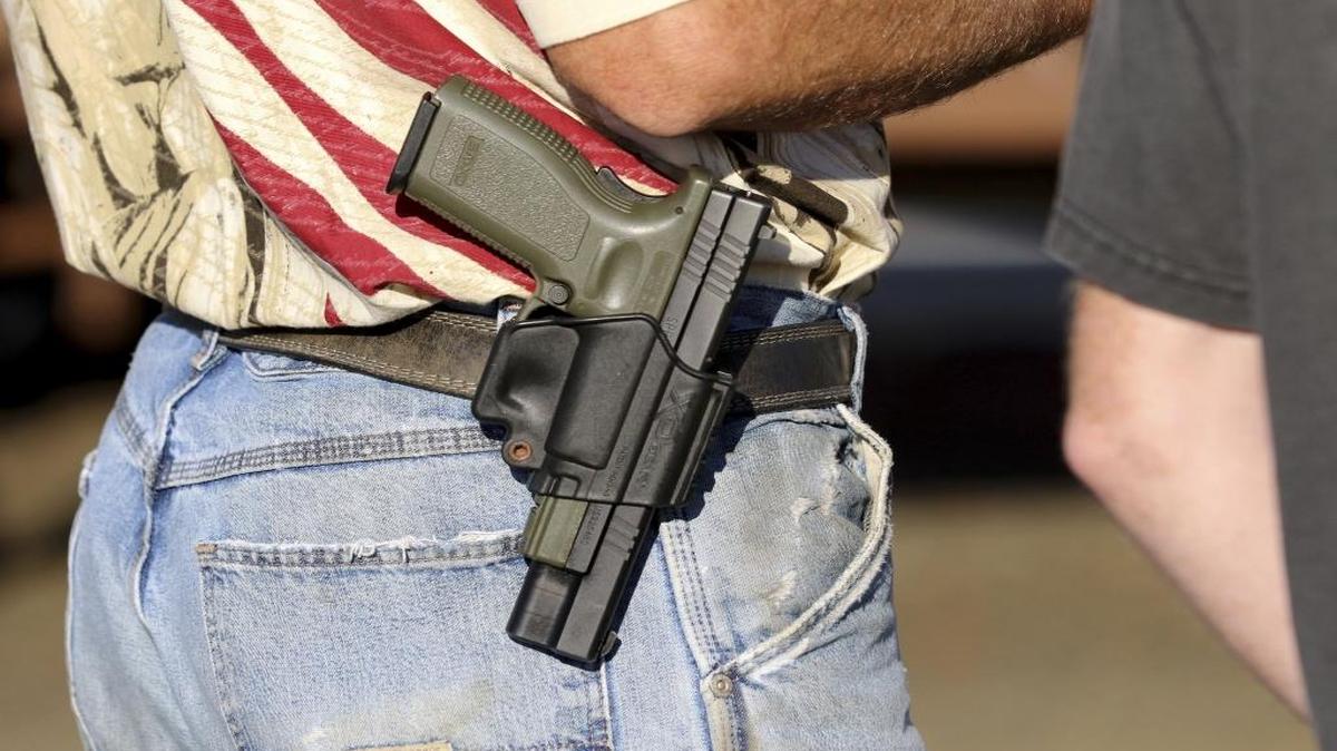 In this Oct. 9, 2015 photo, Michael Johnson wears a firearm as he waits outside of Roseburg Municipal Airport for President Barack Obama's arrival in Roseburg, Ore.