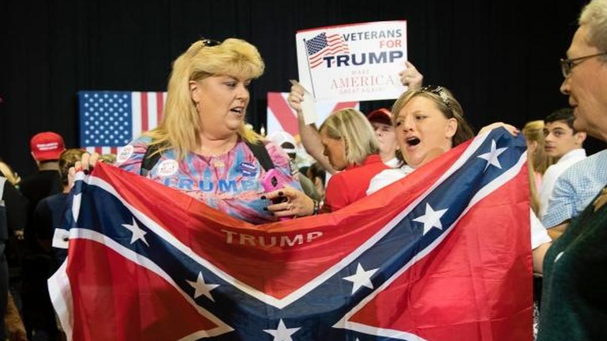Robin Sirois, center left, and Tina Edwards, center right, pose for photographs with a Confederate flag ahead of a Republican presidential candidate Donald Trump campaign stop at the Jacksonville Equestrian Center in Jacksonville, Fla., on Nov. 3.
