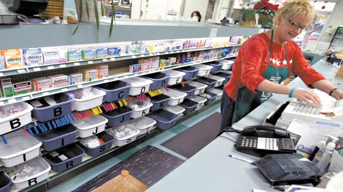 Over the counter medication sits behind the counter as Joyce Hanley takes care of a customer at the Healthplus Pharmacy.