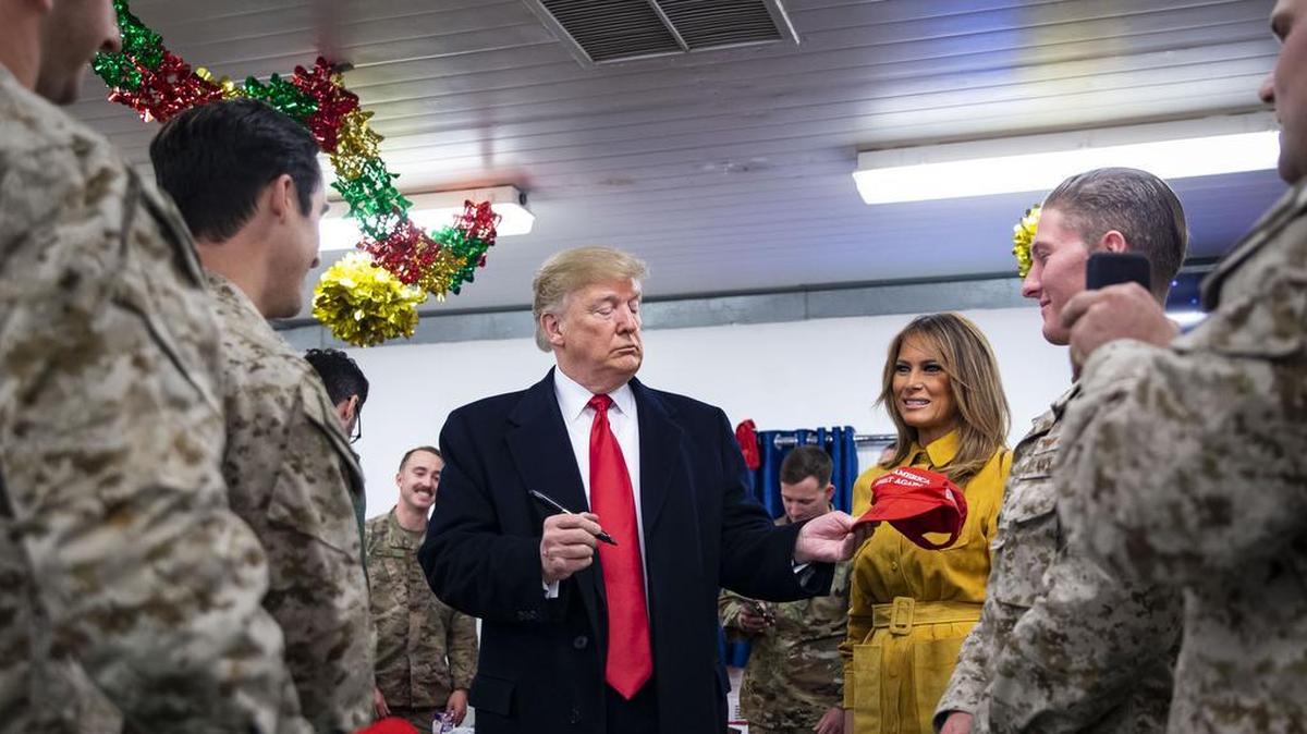 President Donald Trump signs a "Make America Great Again" hat beside first lady Melania Trump as they greet members of the U.S. military in a dining hall, during an unannounced trip at Al Asad Air Base, Iraq, Dec. 26, 2018. Trumps overt politicking in front of active duty troops stationed in Iraq drew heated rebukes from former military officials and Democrats.