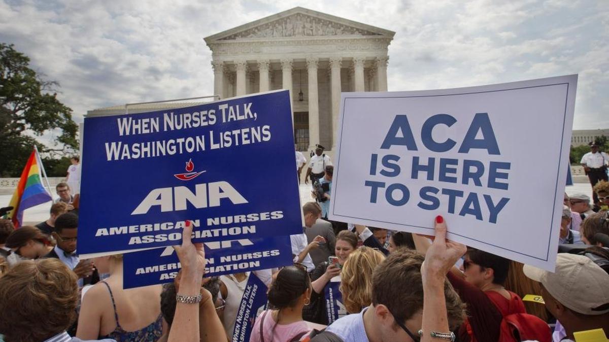 Supporters of the Affordable Care Act hold up signs as the opinion for is reported outside of the Supreme Court in Washington, D.C., on Thursday, June 25, 2015.