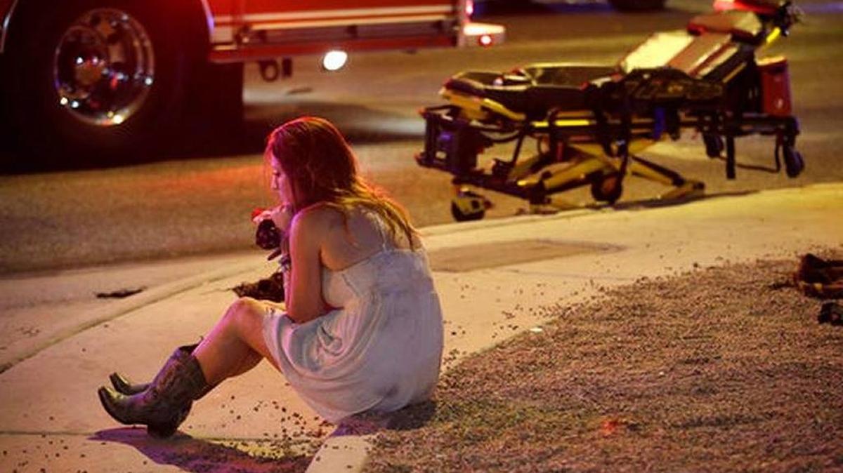 A woman sits on a curb at the scene of a shooting outside of a music festival along the Las Vegas Strip, Monday, Oct. 2, 2017, in Las Vegas. Multiple victims were being transported to hospitals after a shooting late Sunday at a music festival on the Las Vegas Strip.