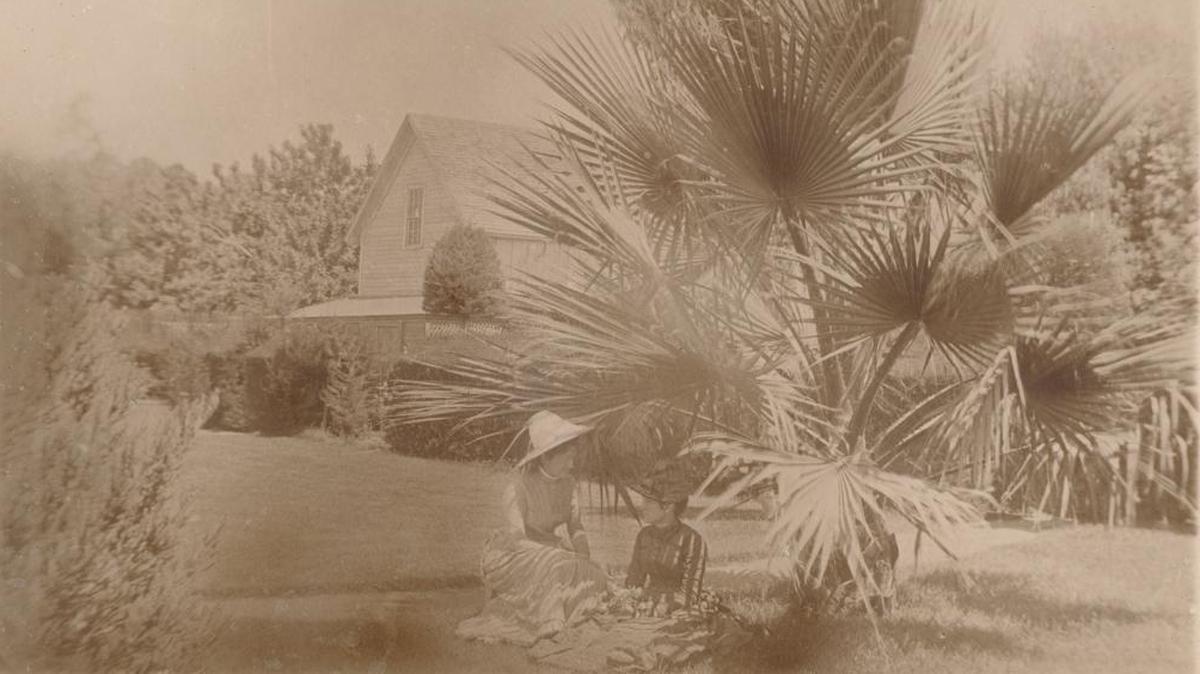 Two women sit in the shade of a palmetto near a carriage house at the Jack House and Gardens in the late 1880s.