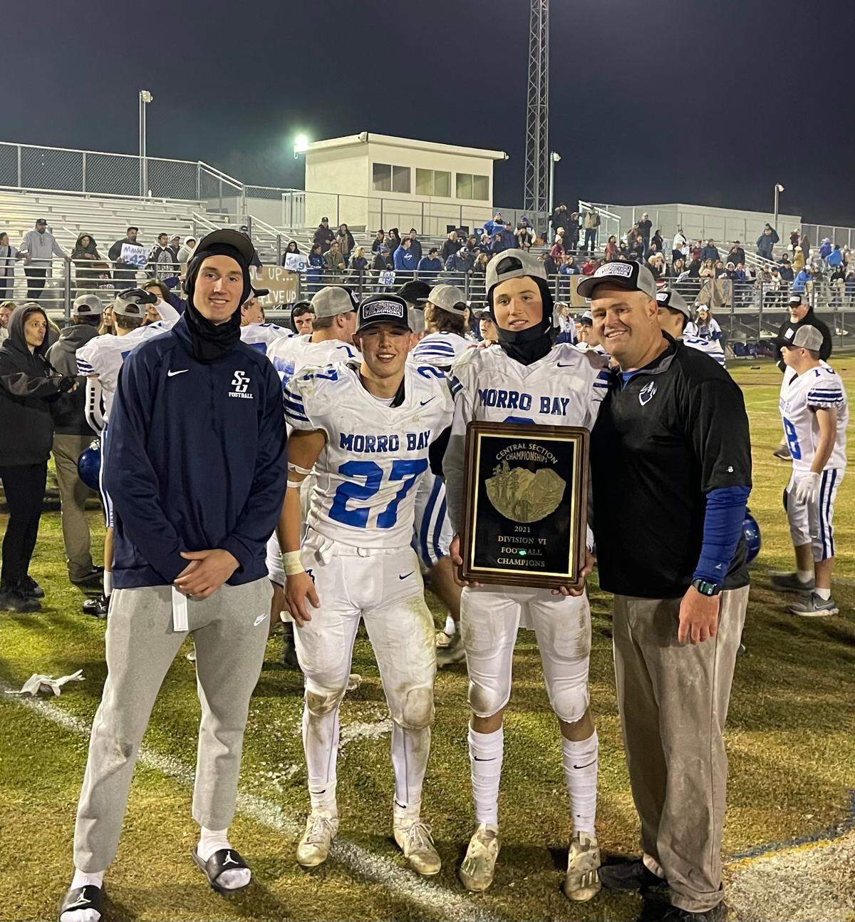 Morro Bay football players Nicky Johnson (holding plaque) and Dylan Turner celebrate their CIF-Central Section Division 6 championship win over Taft on Nov. 26, 2021. Coach Jake Goossen-Brown is standing at right.